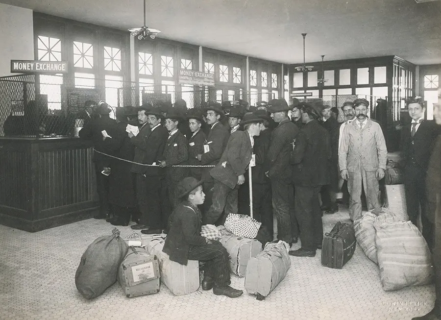 Foto histórica en blanco y negro de un grupo de inmigrantes que ya pasaron el control de la Aduana en la Isla de Ellis -Ellis Island- y hacen fila para cambiar moneda antes de seguir su viaje a su destino final en Estados Unidos - Foto de The New York Public Library en Unsplash disponible en https://unsplash.com/photos/MiVrRlSe4BI
