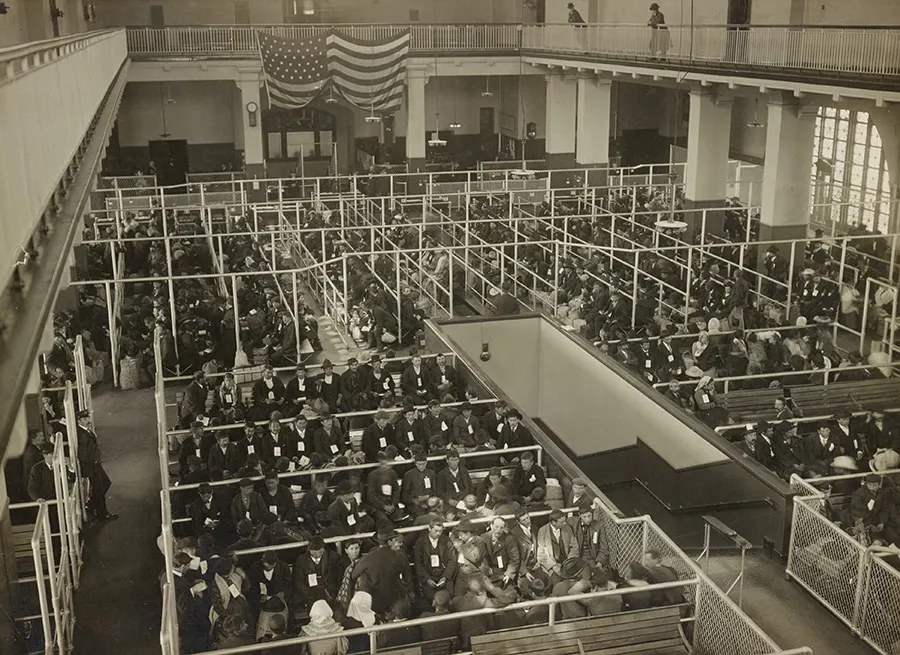 Imagen histórica en blanco y negro de inmigrantes esperando en el Gran Salón de Ellis Island para el control de ingreso de la aduana de Nueva York. Foto de The New York Public Library en Unsplash disponible en https://unsplash.com/photos/zVFLhNlNj7g