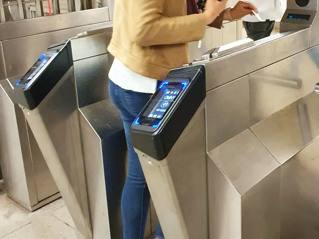 Mujer ingresando por el torniquete a una estación del metro de Nueva York. Se ve en el torniquete la pantalla para hacer tab -pagar- con el sistema OMNY, además la ranura para ingresar con la Metrocard - Foto de Andrea Hoare Madrid