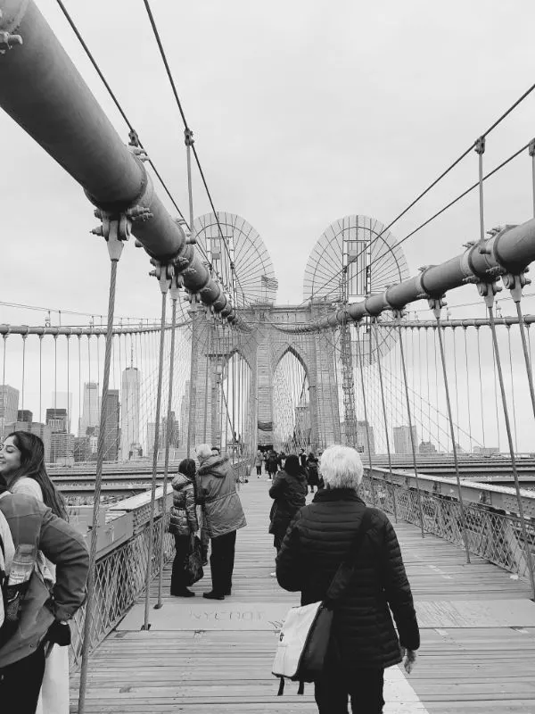 Marina Madrid crossing the Brooklyn Bridge, one of New York's most famous bridges, heading toward Manhattan. Black and white photo by Andrea Hoare Madrid