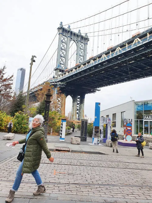 Andrea Hoare walking in front of the entrance to Brooklyn Bridge Park in Dumbo. The Manhattan Bridge is visible in the background. Photo by Marina Madrid