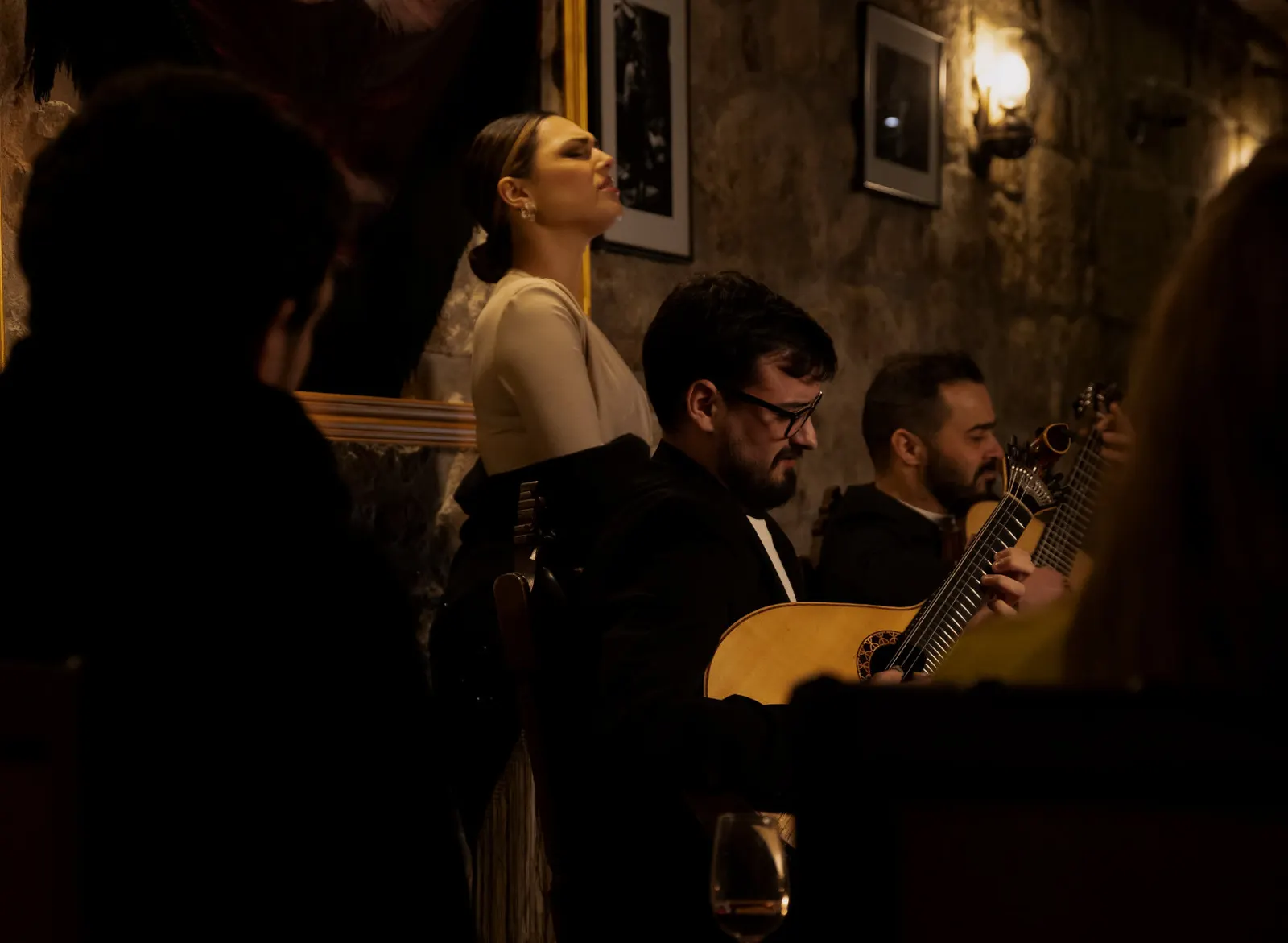 Fado singer and two guitarists performing in the stone-walled room at Fado Maior do Porto