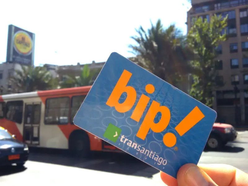 Mano sosteniendo una Tarjeta Bip!, al fondo pasa un bus transitando por la Avenida Alameda a la altura del Colegio de Arquitectos - Foto de Andrea Hoare Madrid