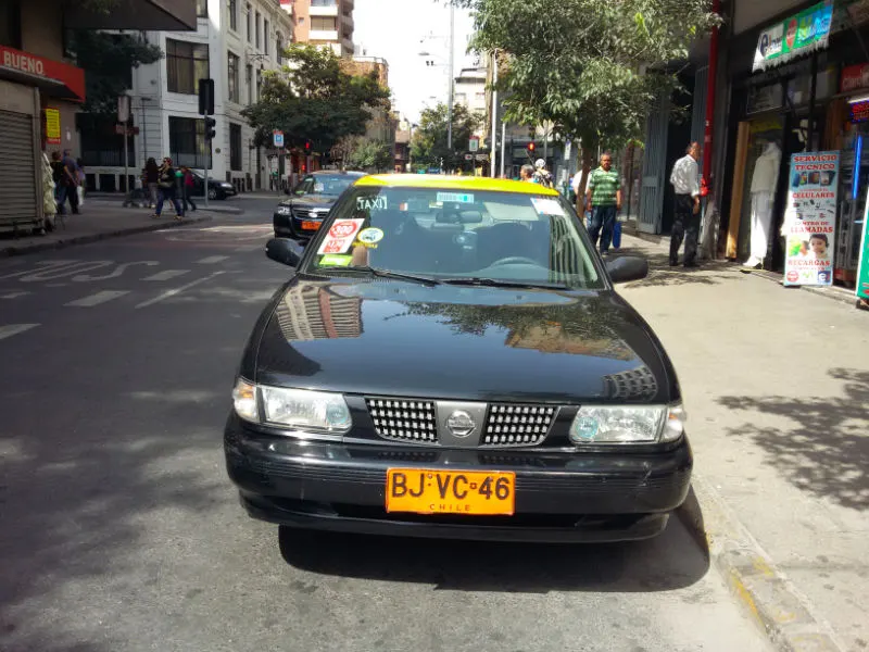 Taxi de Santiago estacionado en una calle del centro, se reconocen por ser negros, techo amarillo y patentes o placas anaranjadas. Foto de AHM