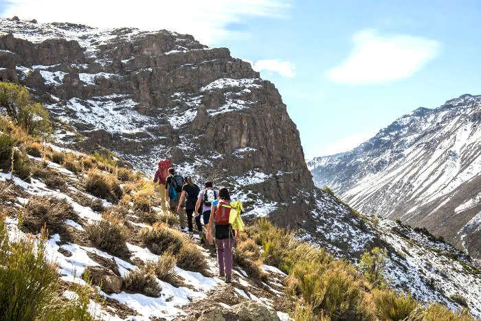 Excursionistas subiendo por una ruta de Trekking del Santuario Yerba Loca cerca de Farellones. Captura de pantalla de la página oficial del parque Yerba Loca disponible en https://yerbaloca.cl/actividades/